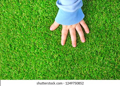 Artificial grass background. Tender hand of a baby on a green artificial turf floor.