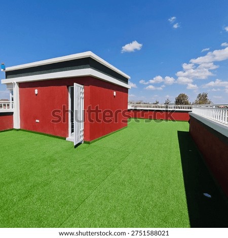 Artificial grass rooftop area featuring a compact red buildin
