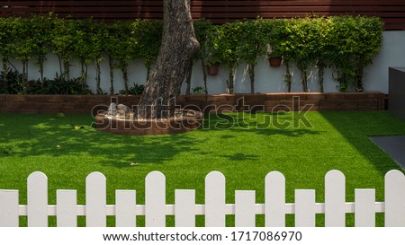 Artificial Grass Turf with Garden House plant in Front Yard area with white wooden Picket Fence on foreground, Home Gardening and exterior architecture concept