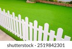 Artificial grass turf with white wooden picket fence in front yard area of vintage house, Home gardening modern design and exterior architecture decoration 