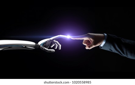 artificial intelligence, future technology and communication concept - robot and human hand connecting fingers on black background with flare