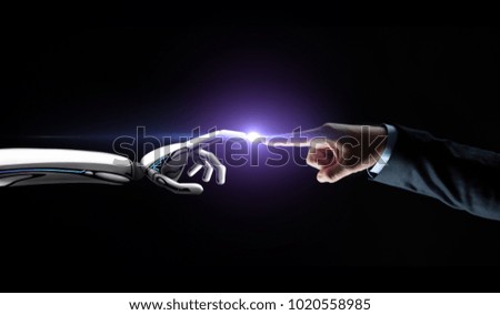 artificial intelligence, future technology and communication concept - robot and human hand connecting fingers on black background with flare