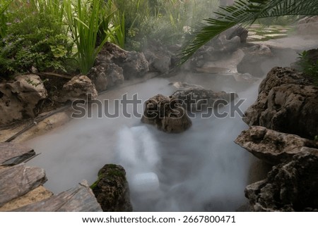 Artificial mist flows between rocks and tropical plants, creating a serene atmosphere in the landscaped garden of TakeTime Glamping, Saraburi, Thailand, on August 11, 2025.