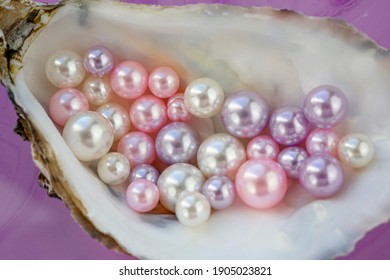 Artificial pearls inside the oyster shell. Different colors and size of pearls. Isolated on a rose background 