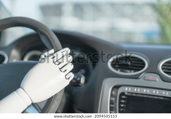 artificial robotic white arm holding steering\
wheel and driving\
vehicle