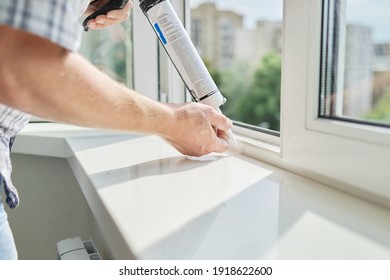 Artificial stone window sill, installation, technological process. Repair, construction of house, apartment. Worker with construction syringe fills seam between sill and window with silicone sealant - Shutterstock ID 1918622600