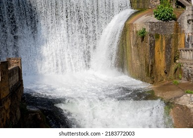 Artificial Waterfall In Garden At The Public Park. Man-made Waterfall In City Park.water In Fountain Falls From The Granite Slabs Down In A Wide Strip.Small Hydroelectric Power Plant Dam Landscape