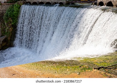 Artificial Waterfall In Garden At The Public Park. Man-made Waterfall In City Park.water In Fountain Falls From The Granite Slabs Down In A Wide Strip.Small Hydroelectric Power Plant Dam Landscape