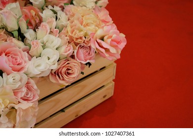 Artificial White And Pink Rose Flowers In Wooden Crate On Red Carpet