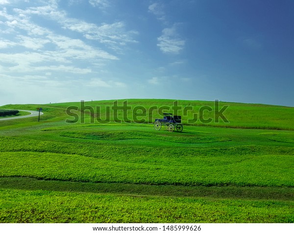 Artificial wood car in the green field and\
blue sky with  clouds. Rural\
landscape.