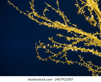 An artificially created tree made from garlands. The branches sparkle with the light of yellow light bulbs against the blue sky - Powered by Shutterstock