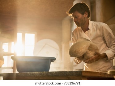 In An Artisan Bakery, A Baker Prepare The Bread Dough. The Morning Sun Comes In Through The Window