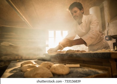 In einer handwerklichen Bäckerei bereitet ein Bäcker den Teig vor. Die Morgensonne kommt durch das Fenster herein