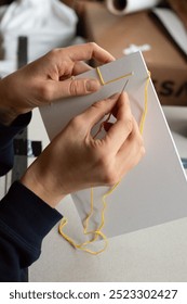 Artisan binding a book using traditional Japanese bookbinding techniques with yellow thread and white paper. The intricate stitching process, minimalist design, handmade craftsmanship.