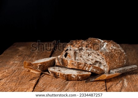 Artisan bread with cut slices on a wooden table. Black background with free space for text.
