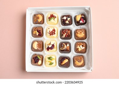 Artisan Handcrafted Chocolate Bonbons Packaged In A Gift Box. Overhead View Of Mixed Chocolate Candies On Pink Surface. 