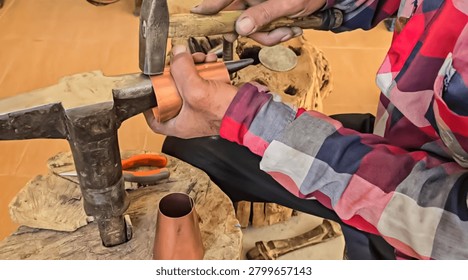 Artisan hands using hammer to shape copper vessel on a metal anvil