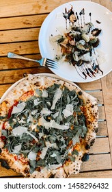 Artisan Oven Fired Pizza With Spinach And Parmesan Cheese On Wooden Table With Side Of Brussel Sprouts Drizzled With Demiglace And A Fork. Shot Outside And Close Up.