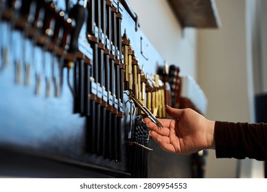 Artisan reaching for a tool on an extensive wall-mounted tool rack in a leathercraft atelier