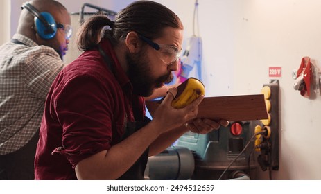 Artisan with safety glasses next to apprentice using sanding block to remove imperfections on wood. Creative man wearing protective gear enjoying diy hobby, using sandpaper to do sanding, camera A - Powered by Shutterstock