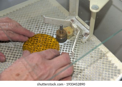 An artisan smooths the edges of cut glass with a grinder.