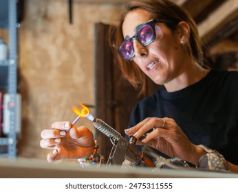 Artisan woman creating a glass jewel with a blowtorch in her artisanal glass workshop - Powered by Shutterstock