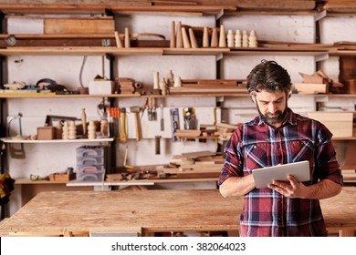 Artisan woodwork studio with shelving holding pieces of wood, with a carpenter standing in his workshop using a digital tablet - Shutterstock ID 382064023