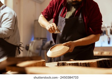 Artisan in woodworking shop pouring brown paint on wood art piece after sanding surface to ensure smoothness, close up. Artist in studio spilling lacquer on wooden bowl to decorate it - Powered by Shutterstock