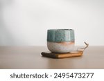 An artisanal cup with teal and speckled glaze poised elegantly on a wooden base, exemplifying minimalist beauty.