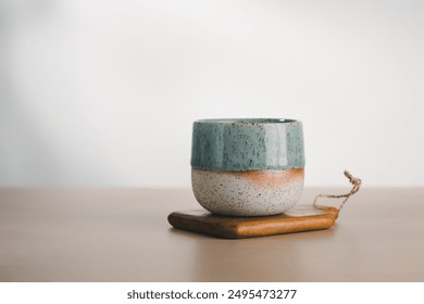 An artisanal cup with teal and speckled glaze poised elegantly on a wooden base, exemplifying minimalist beauty. - Powered by Shutterstock