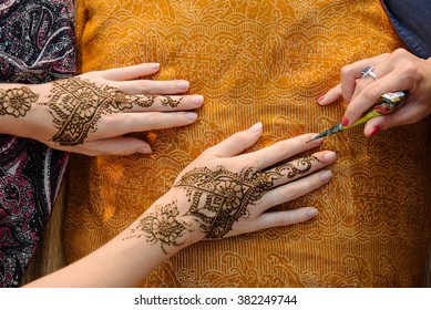 Artist applying henna tattoo on women hands. Mehndi is traditional Indian decorative art. Close-up, top view
