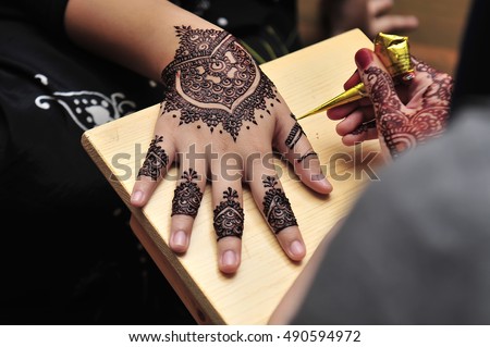 Artist applying henna tattoo on women hands.