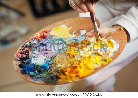 artist brush mix color oil painting on palette is holding in his hand closeup