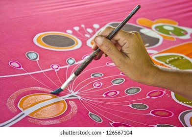 An artist carefully paint the floral/flower motif on a red silk batik fabric