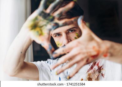 The artist creates a frame with his hands soiled with watercolor paints. Portrait of a young creative artist, the process of creating a picture. - Shutterstock ID 1741251584