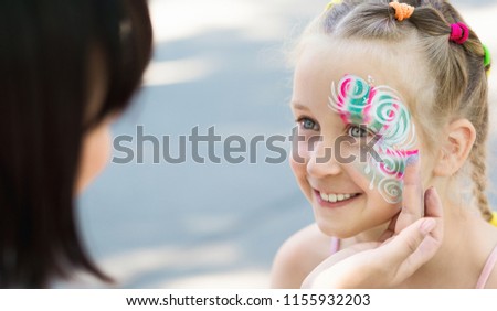 Artist decorating little girl face painting with glitter, happy outdoor walk, copy space
