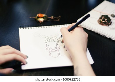 Artist designer girl draws sketch of unusual jewelry ornaments with a pen on white paper. Home workshop - Powered by Shutterstock