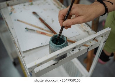 Artist is dipping their paintbrush in a jar of blue paint, preparing to create a work of art - Powered by Shutterstock