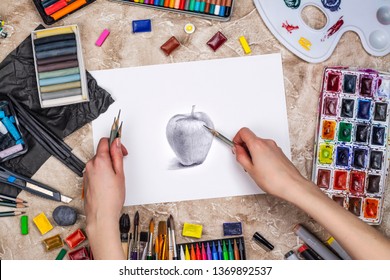 Artist is drawing graphic pencil sketch. Workplace of artist background. Top view of painter tools - pencils, brushes, palette and watercolor paint collection