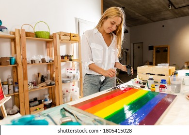 Artist draws LGBT flag adding black color while standing at table in an art Studio