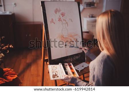 Artist, a European girl, paints painting on canvas with watercolor in her workshop and art school.