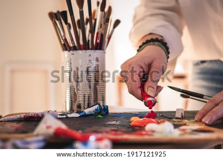 Artist mixing acrylic colors on palette for painting. Woman working in her art studio