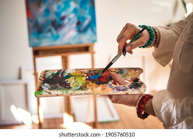 Artist mixing acrylic colors at palette and working on abstract paintings. Woman working in her art studio. Learning creative skill and technique