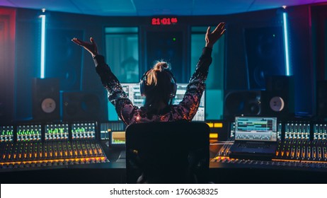 Artist, Musician, Audio Engineer, Producer in Music Record Studio, Uses Control Desk with Computer Screen showing Software UI with Song Playing. Celebrates Success with Raised Hands, Dances. Back View - Powered by Shutterstock