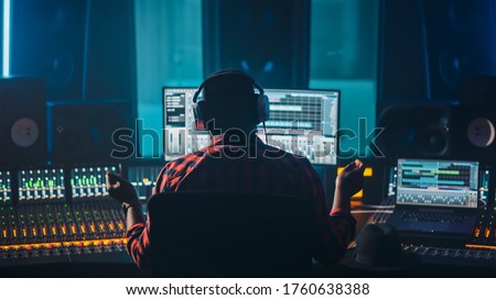 Artist, Musician, Audio Engineer, Producer in Music Record Studio, Uses Control Desk with Computer Screen showing Software UI with Song Playing. Success with Raised Hands, Dances. Back View.