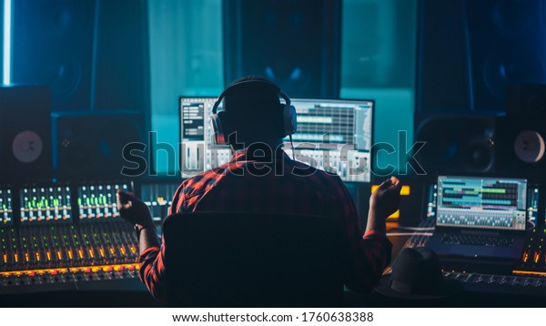 Artist, Musician, Audio Engineer, Producer in Music\
Record Studio, Uses Control Desk with Computer Screen showing\
Software UI with Song Playing. Success with Raised Hands, Dances.\
Back View.