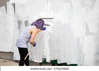 Artist Painting Over Graffiti On A Building Wall