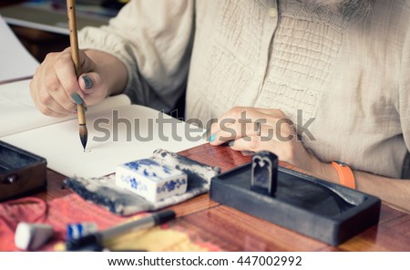 Artist painting in a traditional Japanese technique Sumi-e with Suiteki Water Dropper and sudzuri ink stone. Soft focus on artwork and hands. Art background