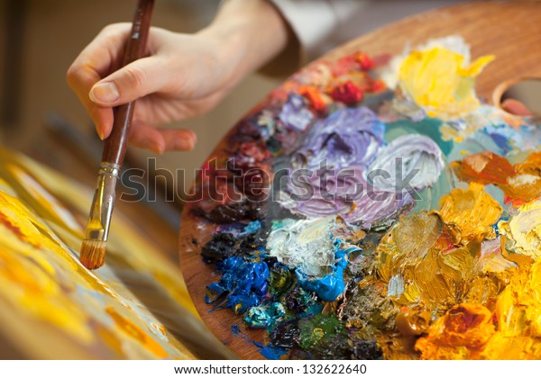 artist paints a picture of oil paint brush in\
hand with palette\
closeup