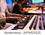 Artist performer recording his song on electronic keyboard piano, working with audio engineer in professional studio and producing new music. Singer composes on synthesizer. Close up.